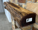 A live edge style fireplace mantel, made from walnut wood, mounted to a rock wall.