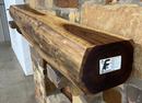 A live edge style fireplace mantel, made from walnut wood, mounted to a rock wall.