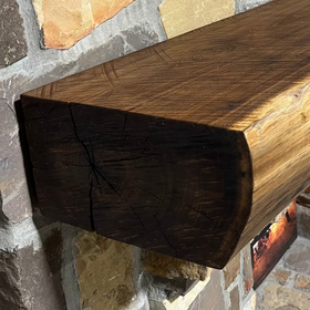 A live edge style fireplace mantel, made from walnut wood, mounted to a rock wall.