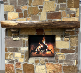 A live edge style fireplace mantel, made from walnut wood, mounted to a rock wall.