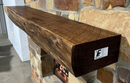 A live edge style fireplace mantel, made from walnut wood, mounted to a rock wall.