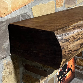 A live edge style fireplace mantel, made from walnut wood, mounted to a rock wall.