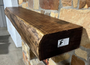 A live edge style fireplace mantel, made from walnut wood, mounted to a rock wall.