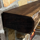A live edge style fireplace mantel, made from walnut wood, mounted to a rock wall.