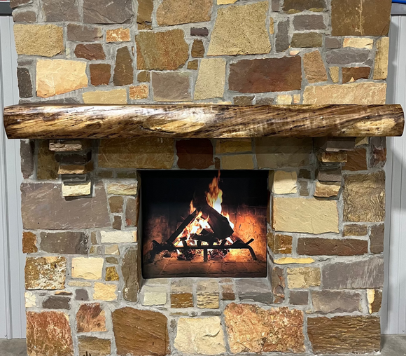 A live edge style fireplace mantel, made from walnut wood, mounted to a rock wall.