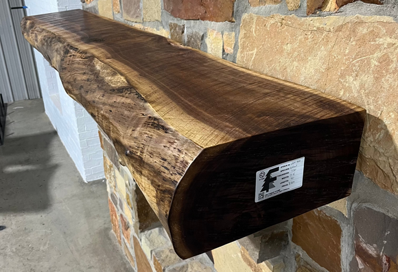 A live edge style fireplace mantel, made from walnut wood, mounted to a rock wall.