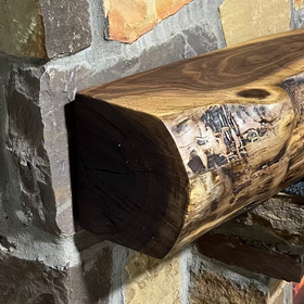 A live edge style fireplace mantel, made from walnut wood, mounted to a rock wall.