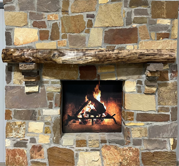 A live edge style fireplace mantel, made from walnut wood, mounted to a rock wall.