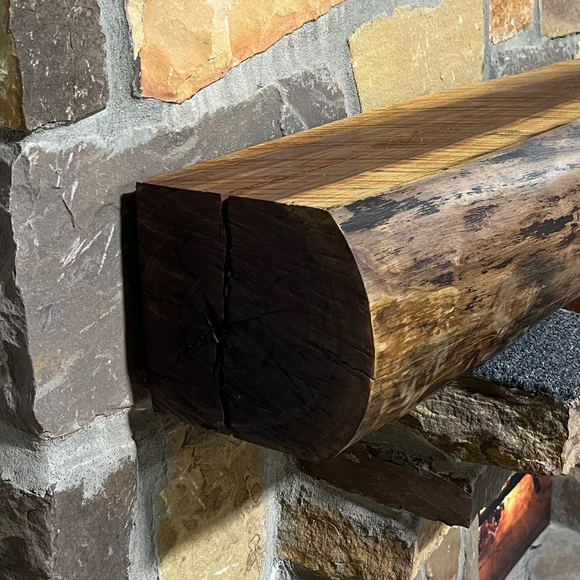 A live edge style fireplace mantel, made from walnut wood, mounted to a rock wall.