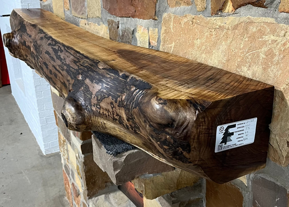 A live edge style fireplace mantel, made from walnut wood, mounted to a rock wall.