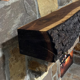 A live edge style fireplace mantel, made from walnut wood, mounted to a rock wall.