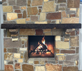 A live edge style fireplace mantel, made from walnut wood, mounted to a rock wall.