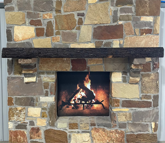 A live edge style fireplace mantel, made from walnut wood, mounted to a rock wall.