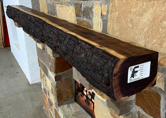 A live edge style fireplace mantel, made from walnut wood, mounted to a rock wall.