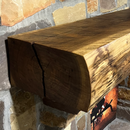 A live edge style fireplace mantel, made from walnut wood, mounted to a rock wall.