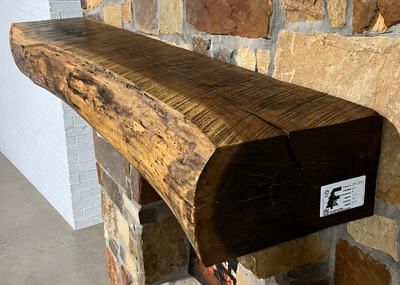 A live edge style fireplace mantel, made from walnut wood, mounted to a rock wall.