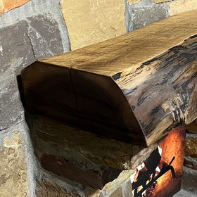A live edge style fireplace mantel, made from walnut wood, mounted to a rock wall.