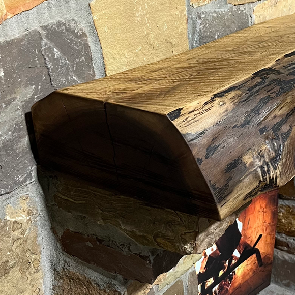 A live edge style fireplace mantel, made from walnut wood, mounted to a rock wall.