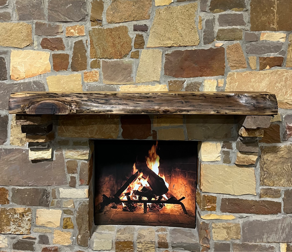 A live edge style fireplace mantel, made from walnut wood, mounted to a rock wall.