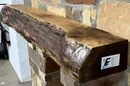 A live edge style fireplace mantel, made from walnut wood, mounted to a rock wall.