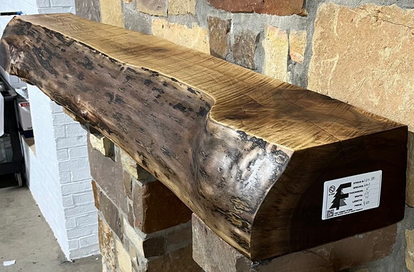 A live edge style fireplace mantel, made from walnut wood, mounted to a rock wall.
