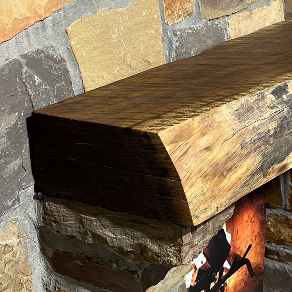 A live edge style fireplace mantel, made from walnut wood, mounted to a rock wall.