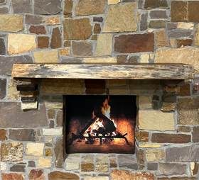 A live edge style fireplace mantel, made from walnut wood, mounted to a rock wall.
