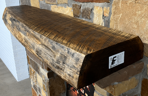 A live edge style fireplace mantel, made from walnut wood, mounted to a rock wall.