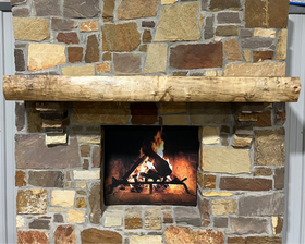 A live edge style fireplace mantel, made from walnut wood, mounted to a rock wall.