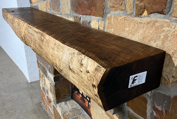 A live edge style fireplace mantel, made from walnut wood, mounted to a rock wall.