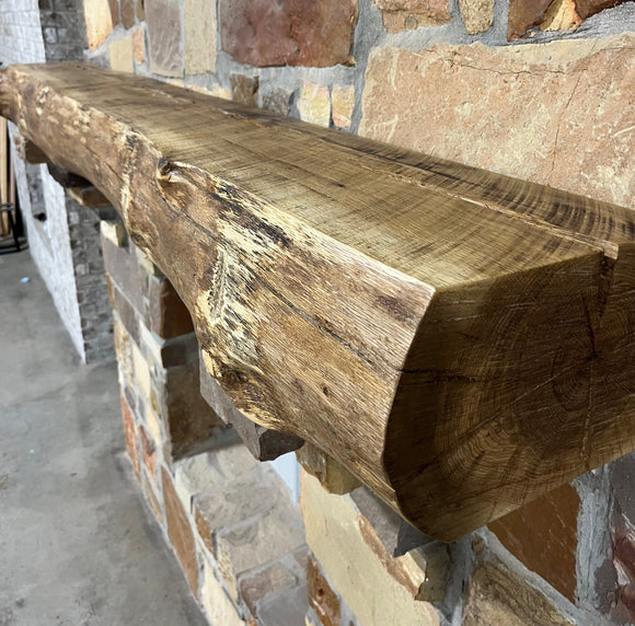 A live edge style fireplace mantel, made from white oak wood, mounted on a stone wall.