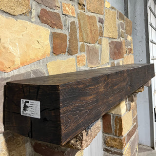 A burnt oak solid wood beam fireplace mantel on a rock fireplace