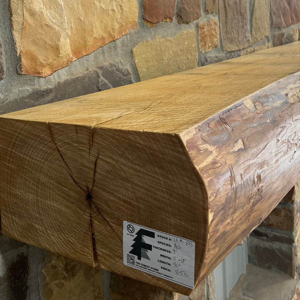Solid live edge ash fireplace mantel mounted on a stone wall.