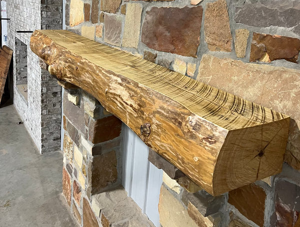 Solid live edge ash fireplace mantel mounted on a stone wall.