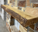 Solid live edge ash fireplace mantel mounted on a stone wall.