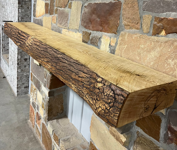 Solid live edge ash fireplace mantel mounted on a stone wall.