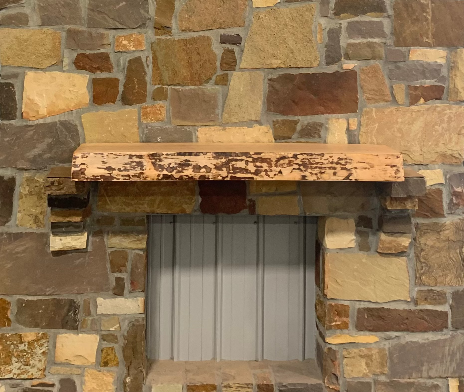 Solid live edge birch fireplace mantel mounted on a stone wall