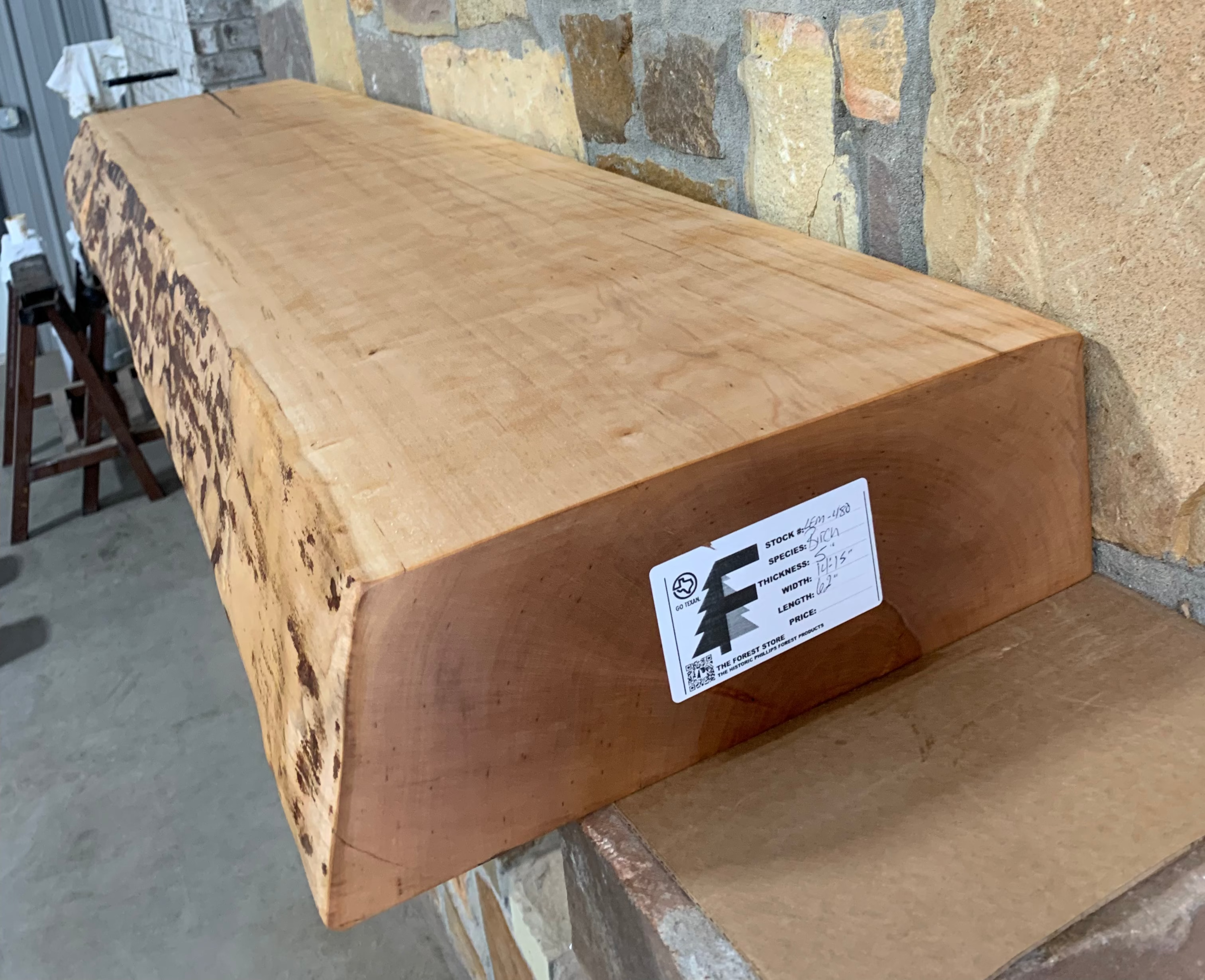 Solid live edge birch fireplace mantel mounted on a stone wall