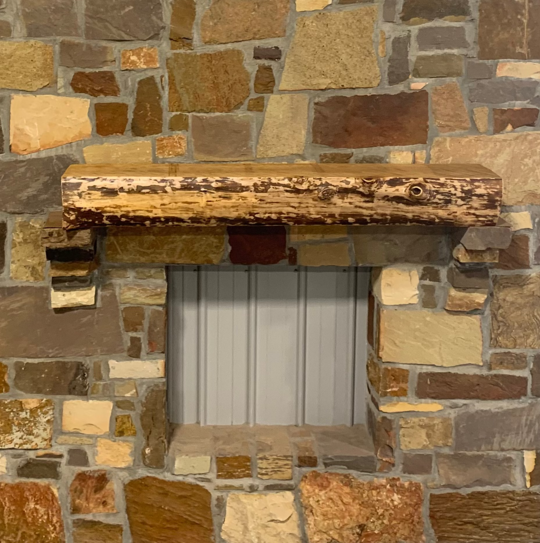 Solid live edge birch fireplace mantel mounted on a stone wall