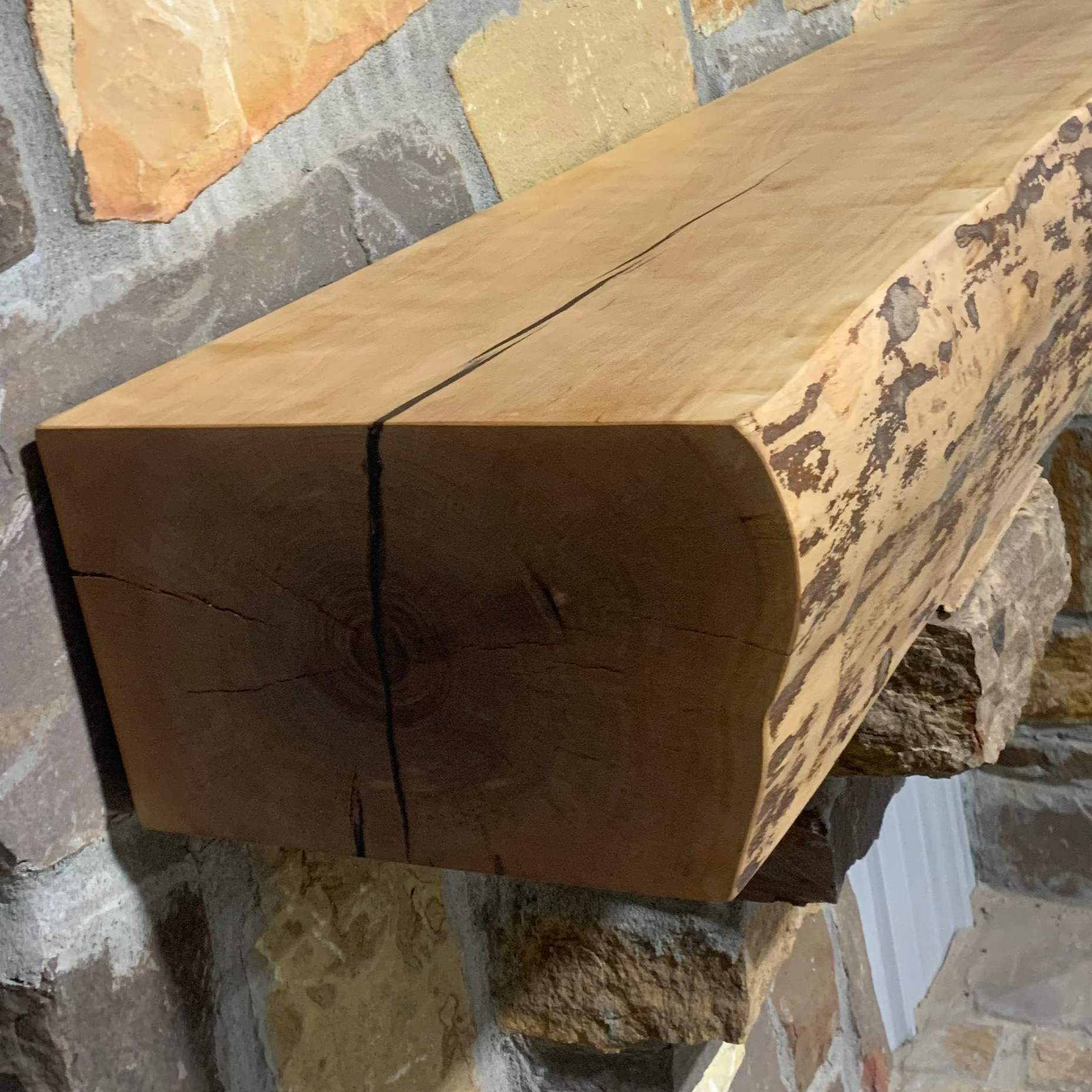Solid live edge birch fireplace mantel mounted on a stone wall