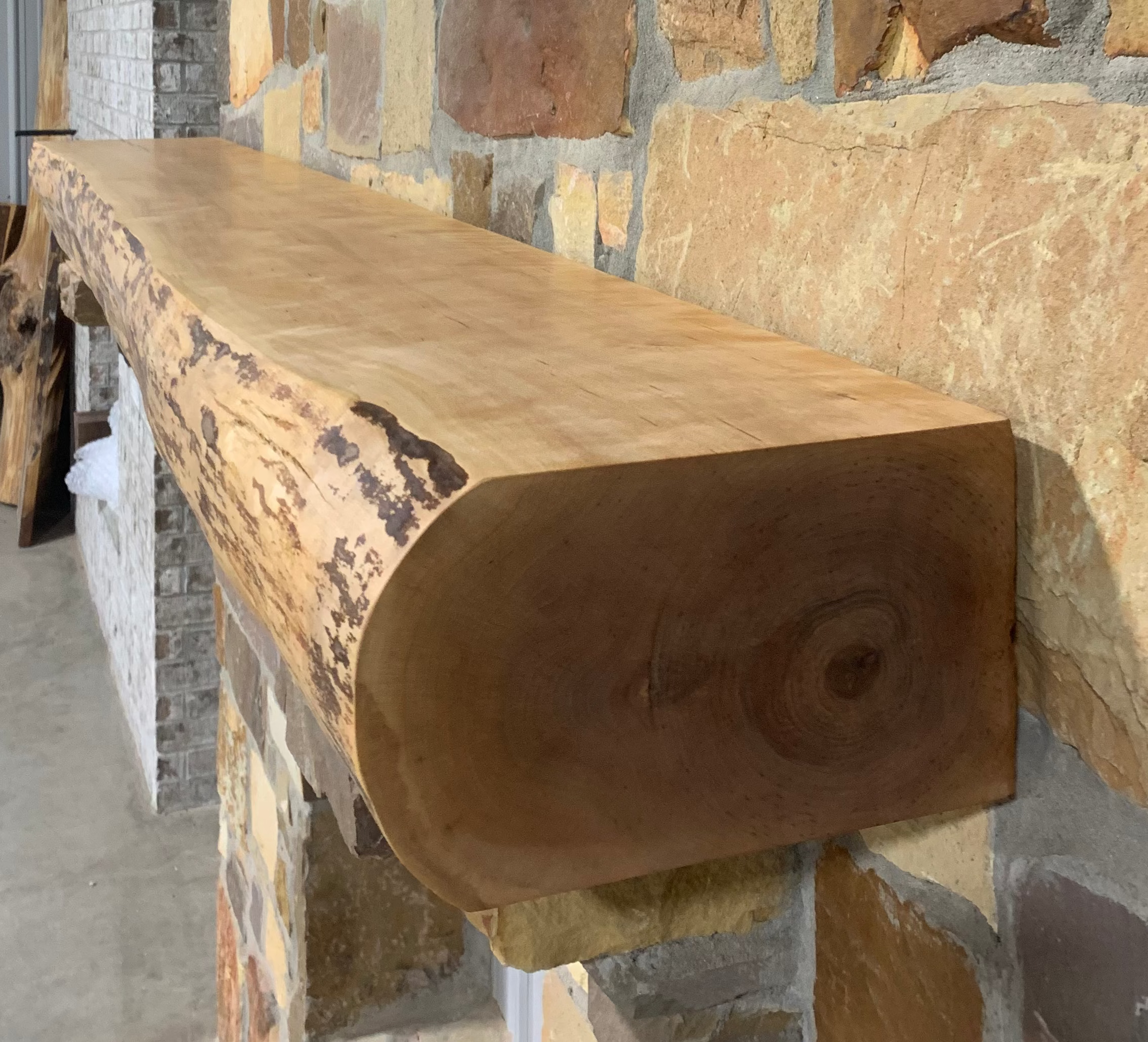 Solid live edge birch fireplace mantel mounted on a stone wall