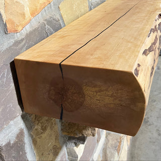Solid live edge birch fireplace mantel mounted on a stone wall.
