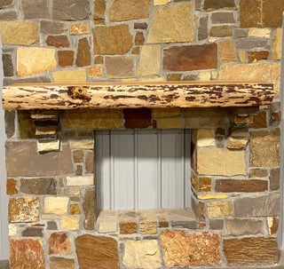 Solid live edge birch fireplace mantel mounted on a stone wall.
