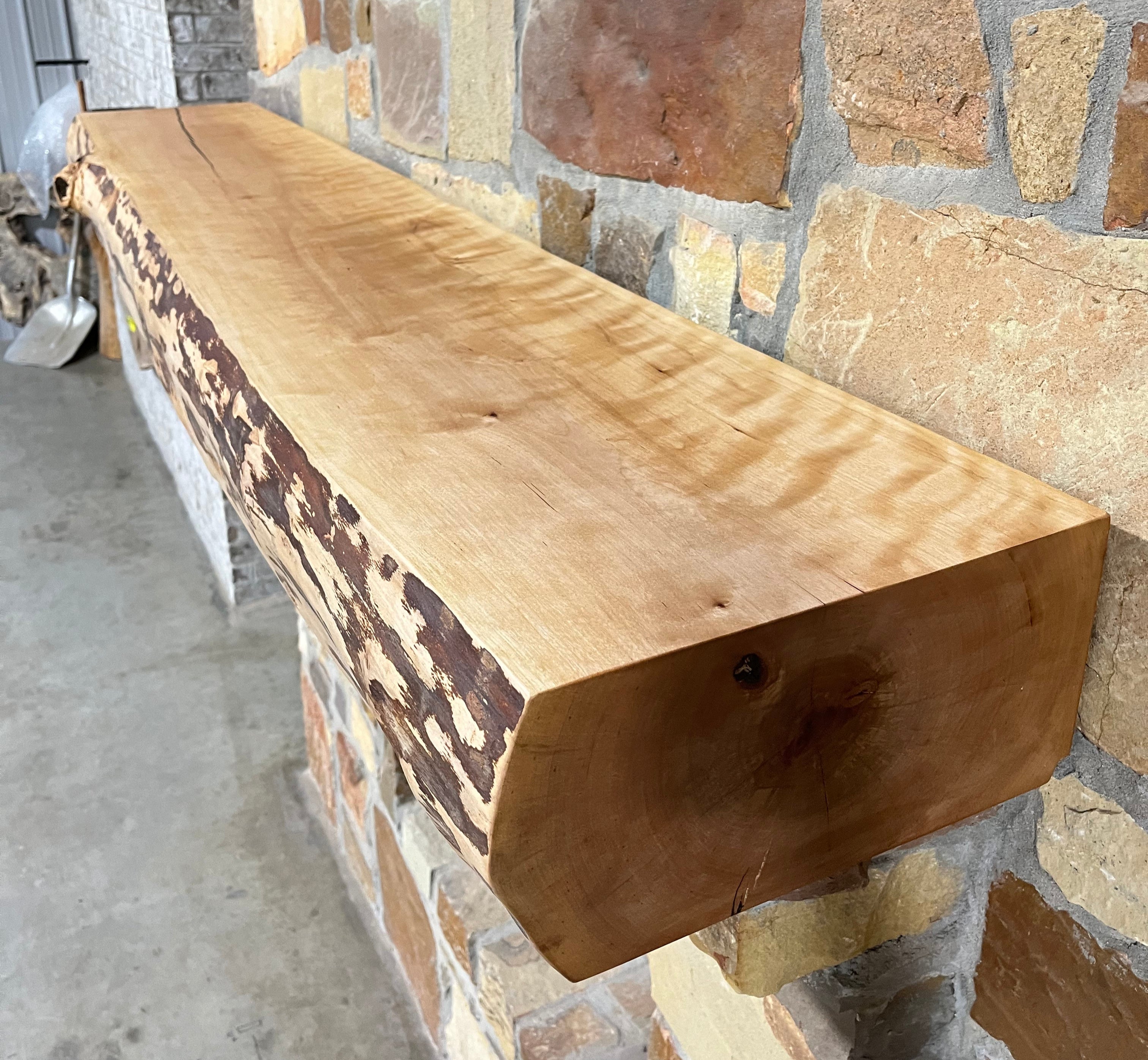 Solid live edge birch fireplace mantel mounted on a stone wall.
