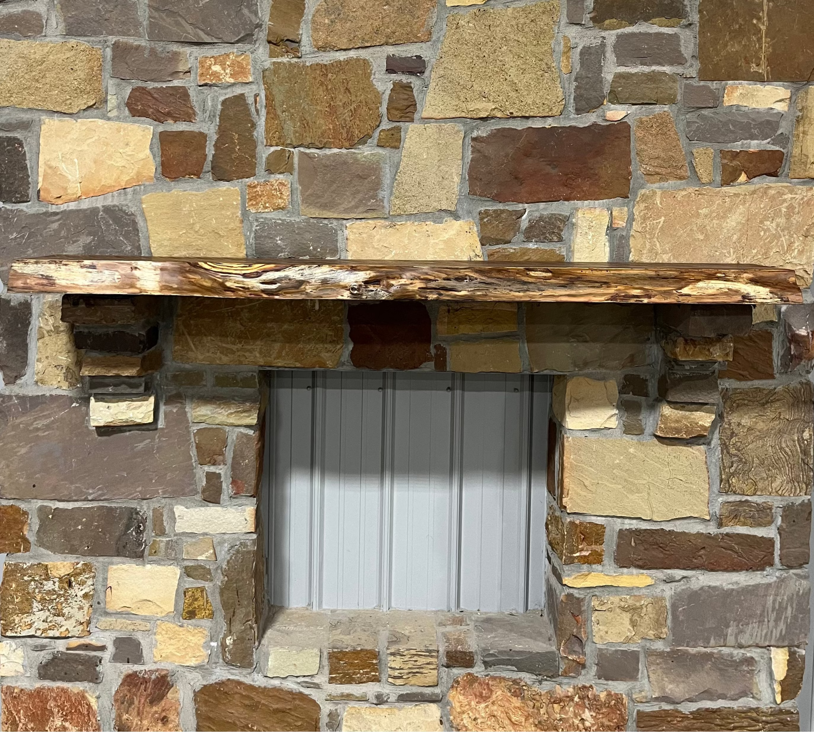 Solid live edge bois d'arc fireplace mantel mounted on a stone wall.

