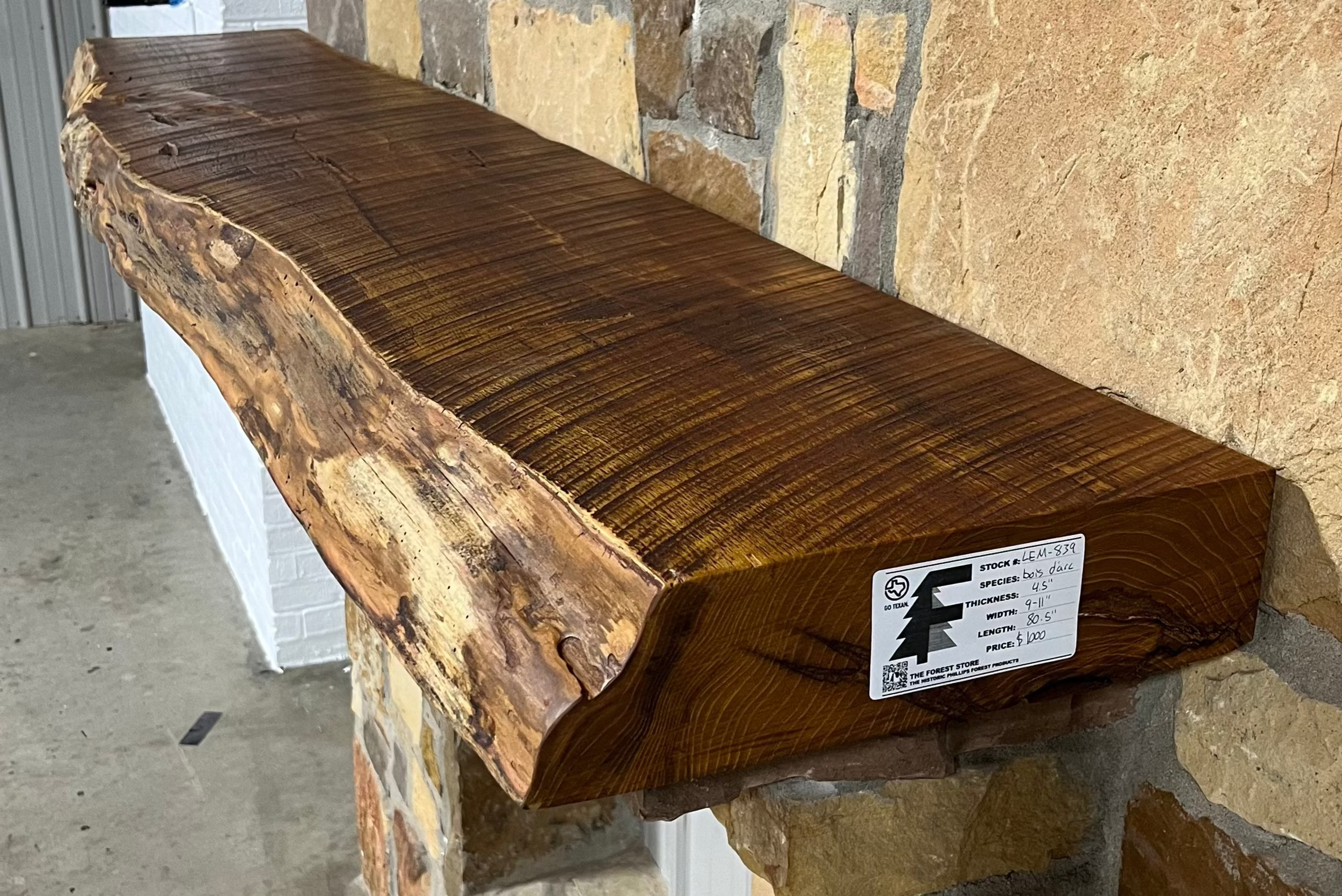 Solid live edge bois d'arc fireplace mantel mounted on a stone wall.
