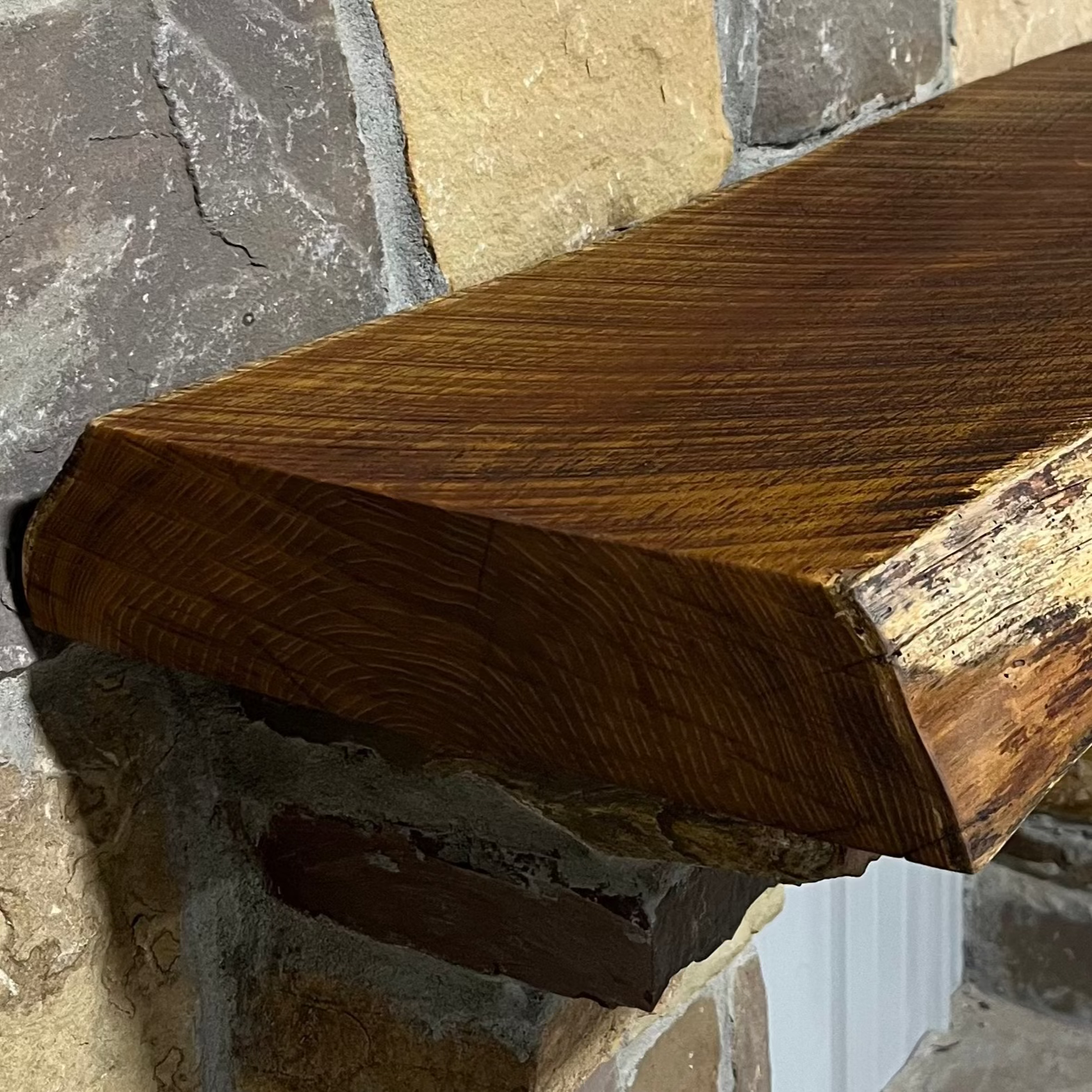 Solid live edge bois d'arc fireplace mantel mounted on a stone wall.
