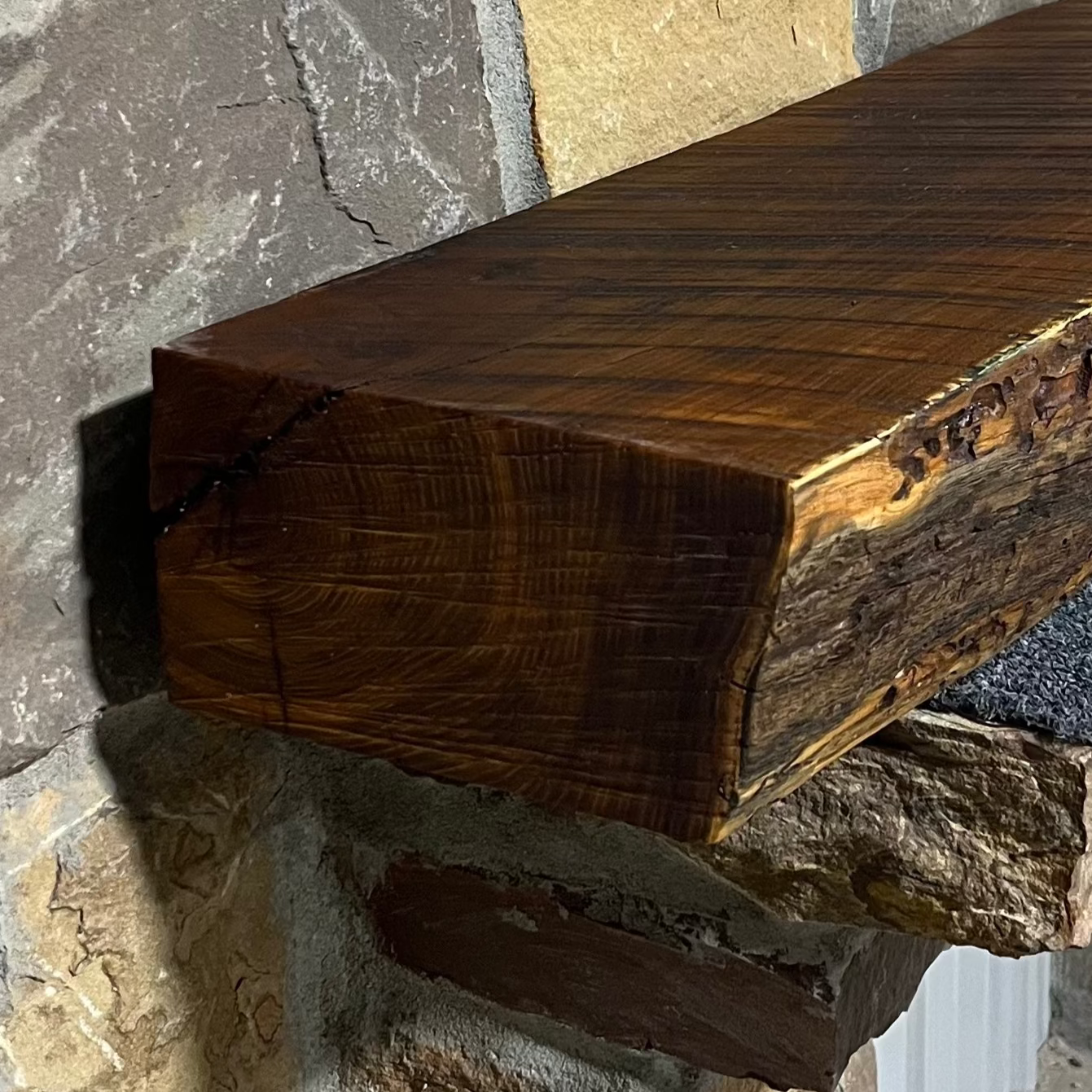 Solid live edge bois d'arc fireplace mantel mounted on a stone wall.
