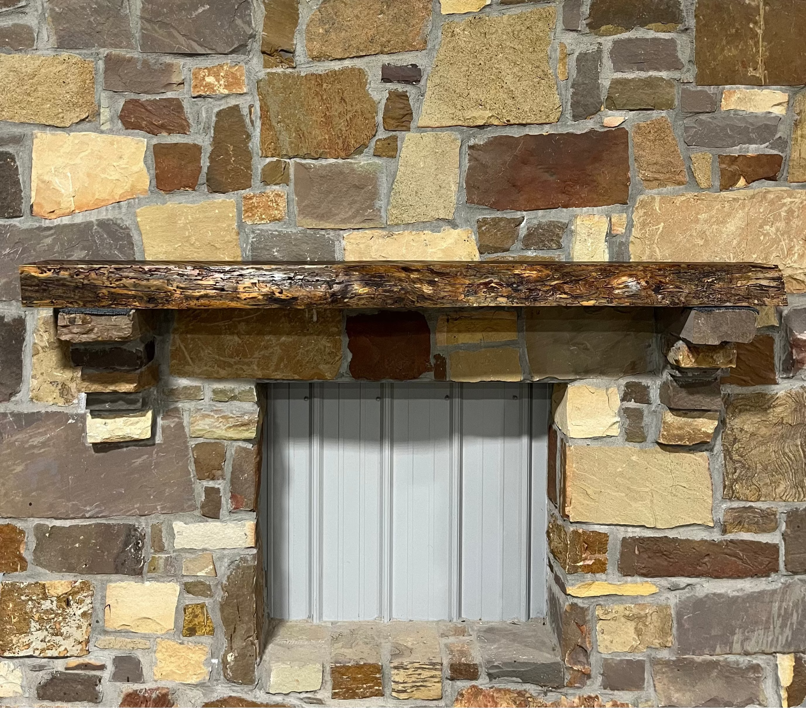 Solid live edge bois d'arc fireplace mantel mounted on a stone wall.
