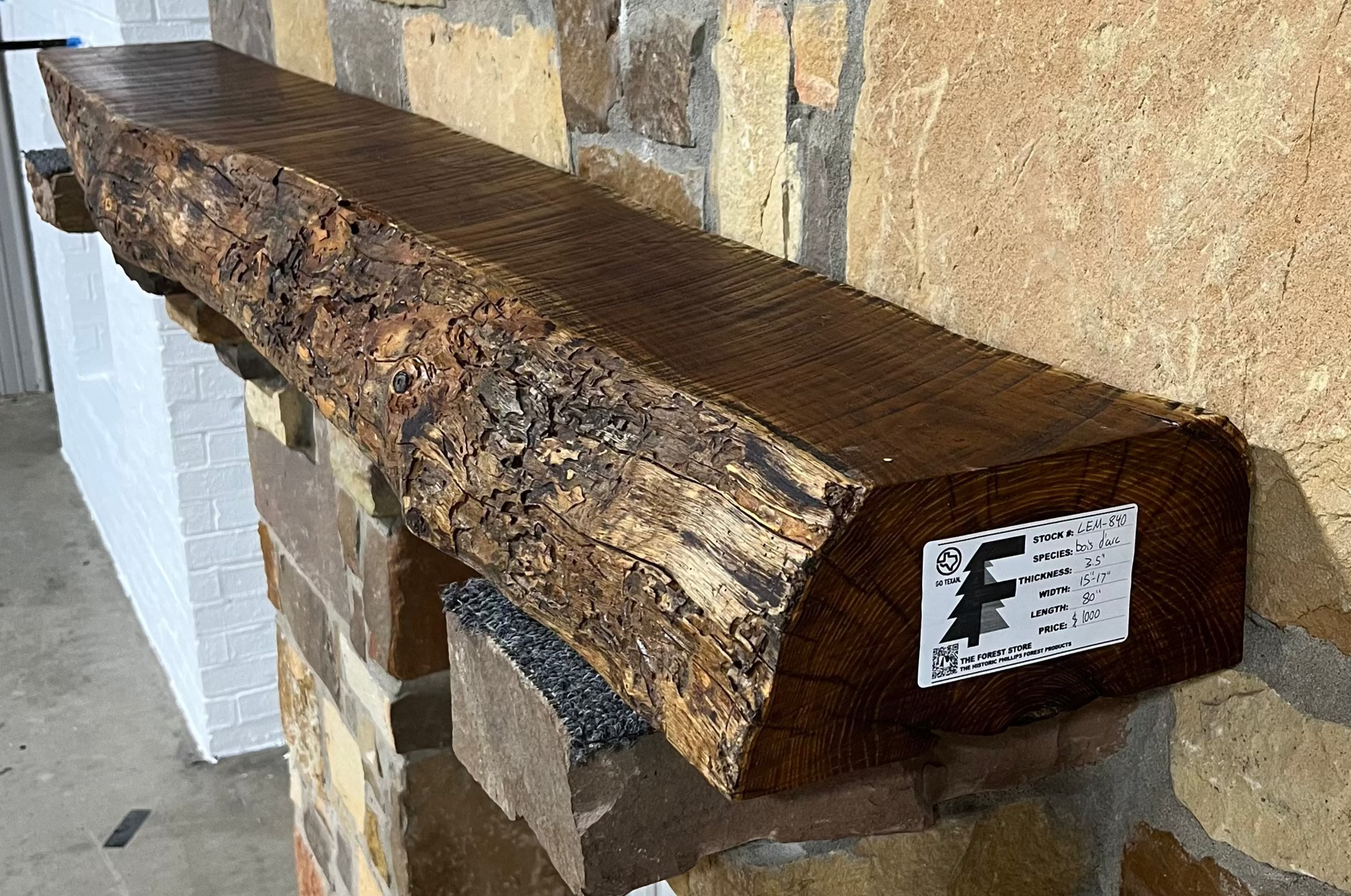Solid live edge bois d'arc fireplace mantel mounted on a stone wall.
